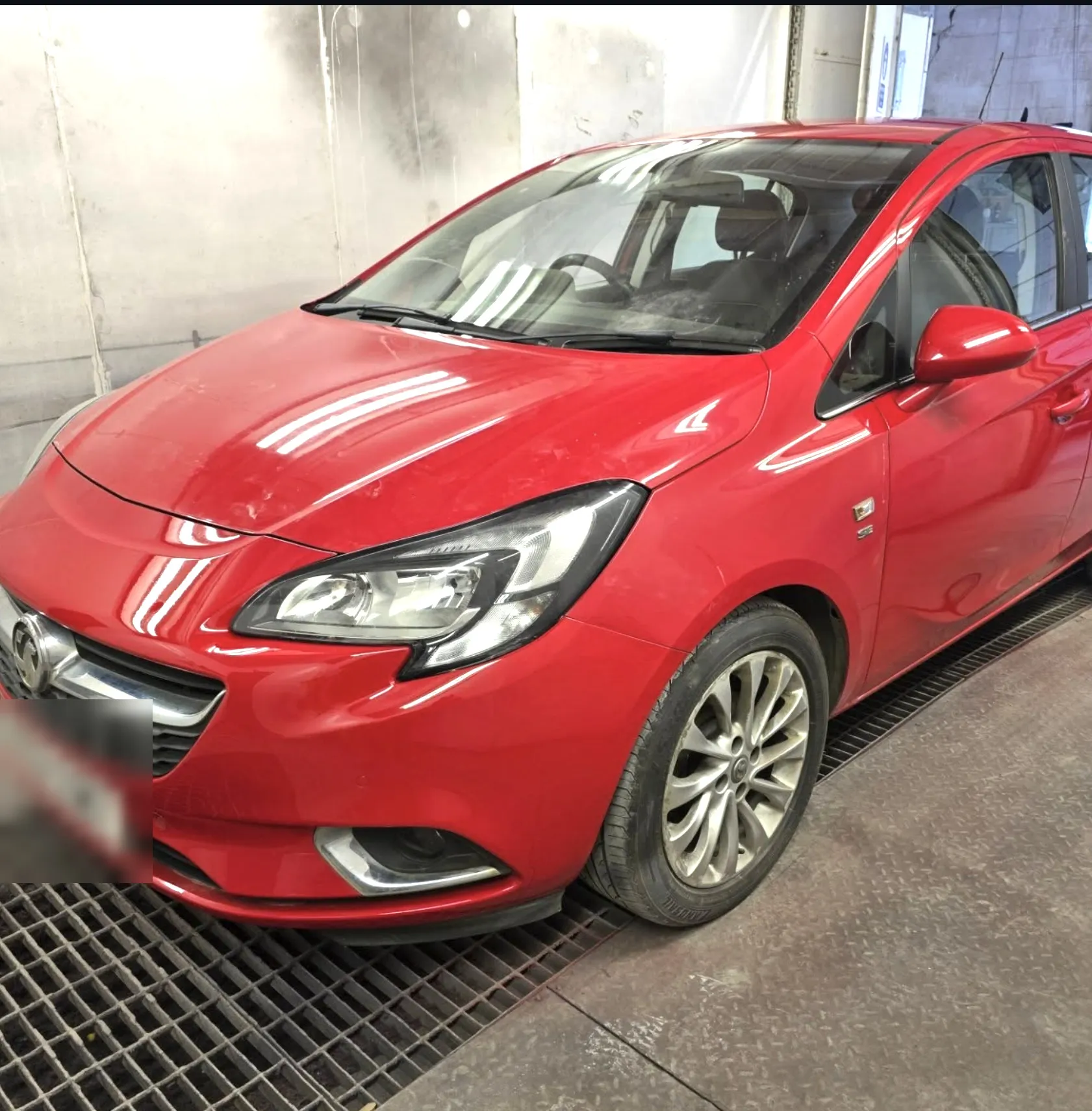 Red Vauxhall Corsa with a freshly finished front bumper, standing on the grated floor of the workshop bay.